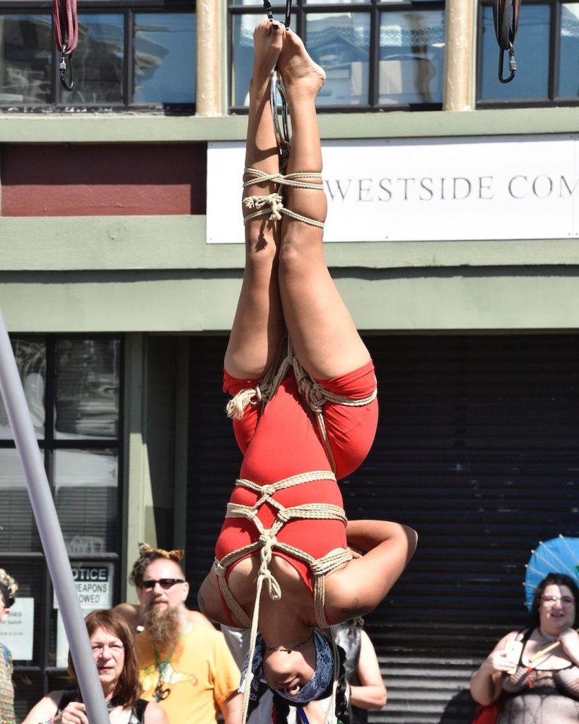 A person hanging upside down in bondage gear.