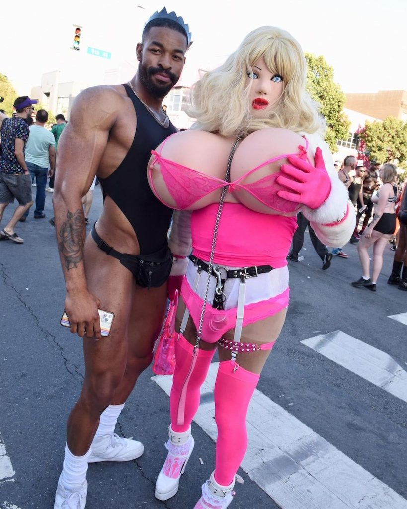 Two people, the person on the right is in a costume that has fake breasts.