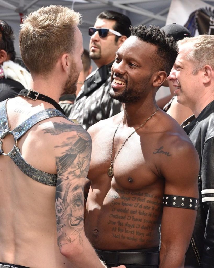 Two shirtless men smiling at each other.