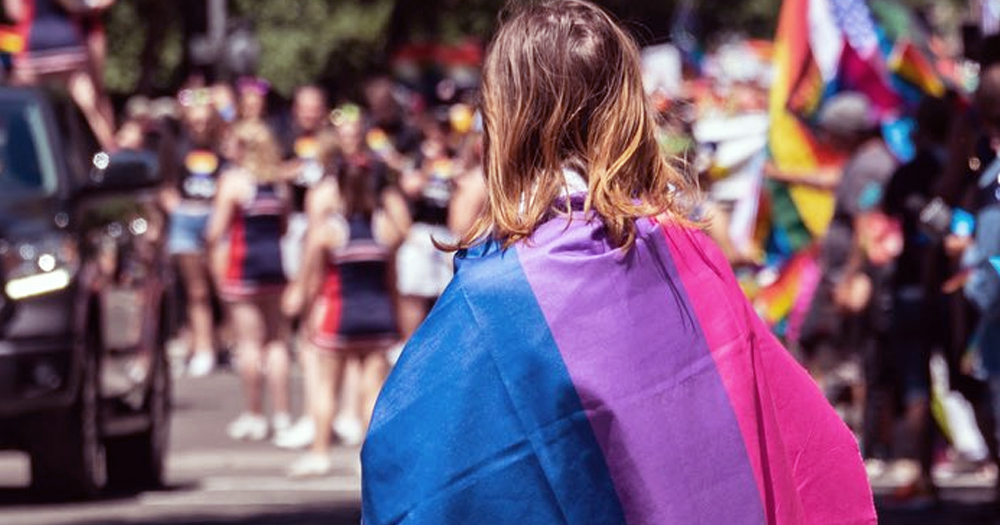 This article is about the impact of biphobia on the lives of bisexual people. In the picture, a person wearing a Bi Pride flag at Pride march.
