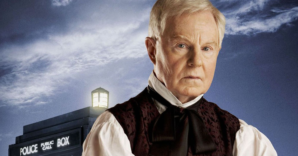 The image shows Derek Jacobi in a Victorian style blouse and waistcoat standing in front of the Doctor Who Tardis.