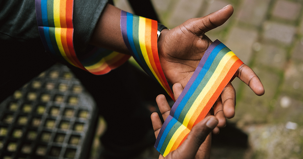 A person is holding a pride ribbon wrapped around their hands.
