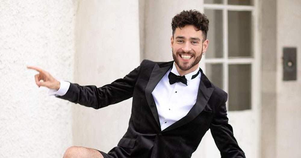 The image shows Tenor Seán Kennedy wearing a tuxedo with his arms out stretched leaning to the side smiling.