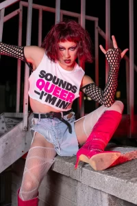 A drag queen wearing a 'Sounds Queer I'm In' t-shirt from the new GCN collection.