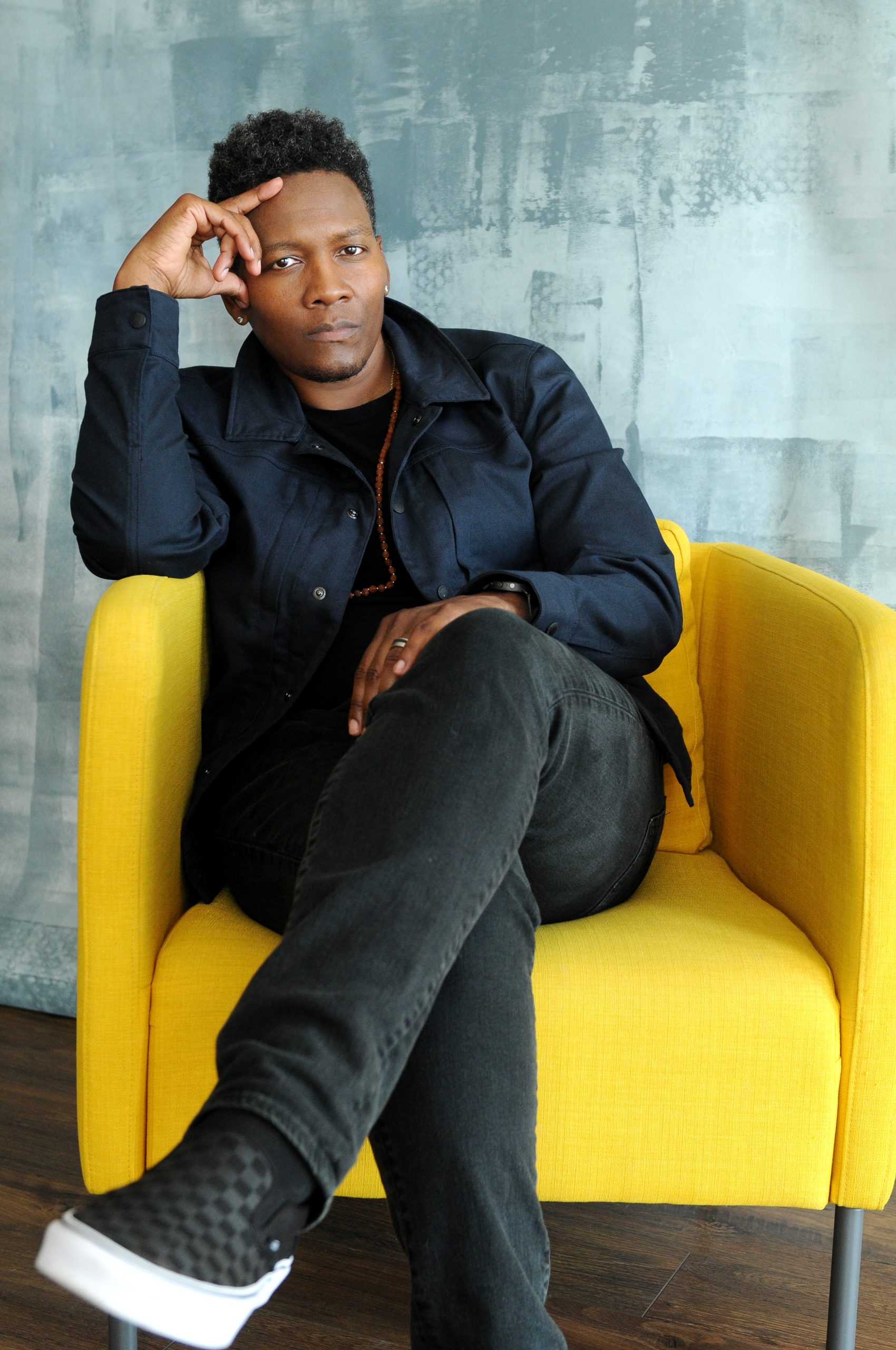 An image of Lea sitting down looking towards the camera with their legs crossed.