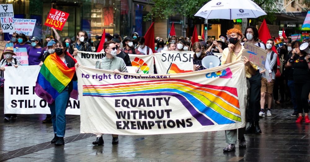 Photo of a street protest where three people are holding an "equality without exemptions" poster protesting in favour of polyamorous relationships