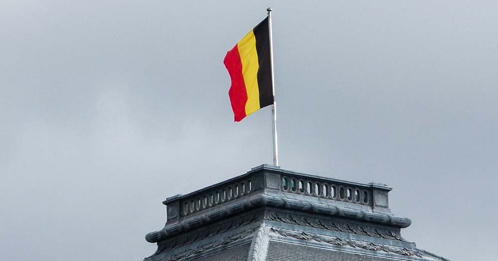 Belgium flag waving over government building representing plans to ban conversion therapy.