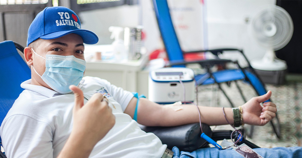 A man in a blue cap and mask donates blood.