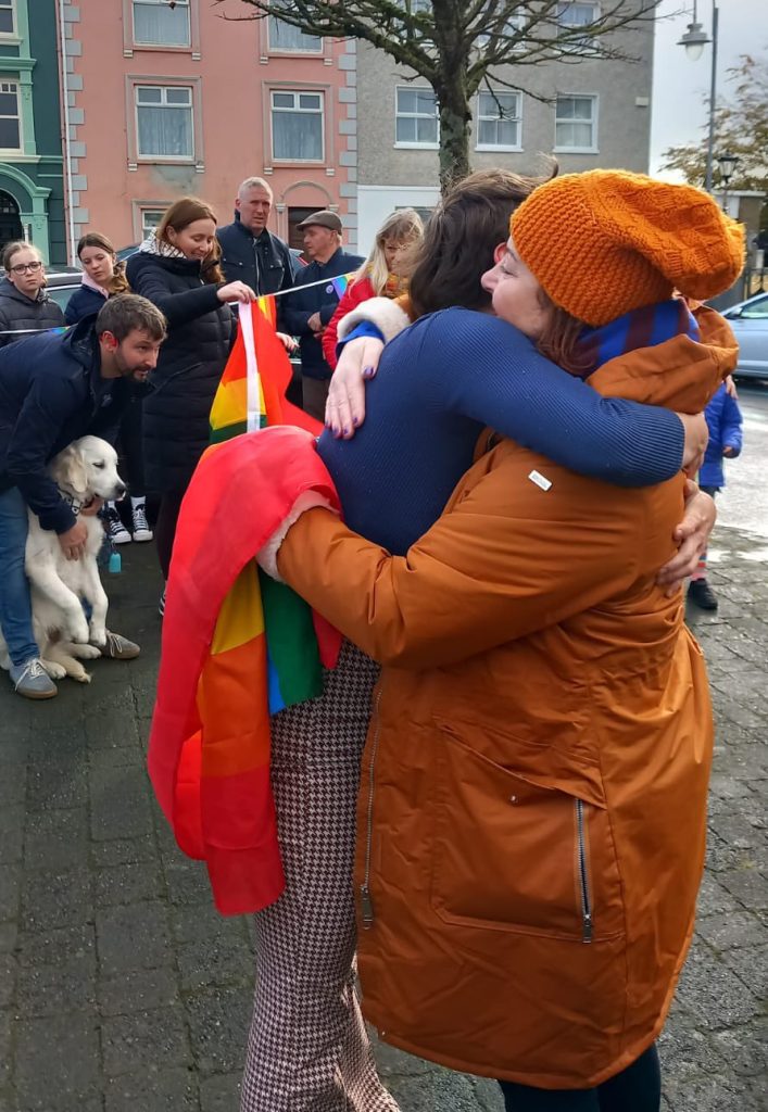 LGBTQ+ campaigners gathered in Listowel in front of St Mary’s Church, holding flowers and Pride flags.
