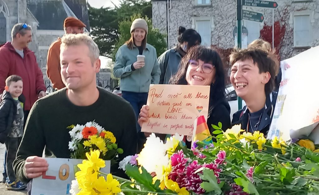 LGBTQ+ campaigners gathered in Listowel in front of St Mary’s Church, holding flowers and Pride flags.