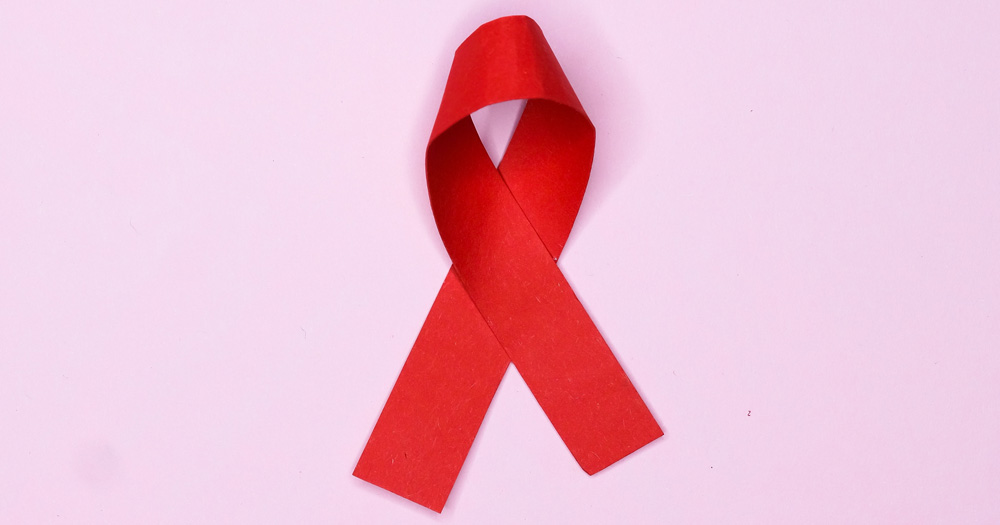A picture of a red ribbon on a pink background, representing HIV/AIDs, an issue to be discussed at the Gay Health Forum 2022.