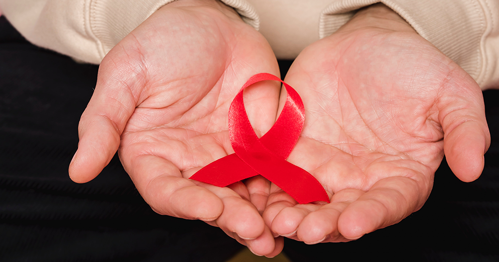 A person holding a HIV red ribbon in their hands.