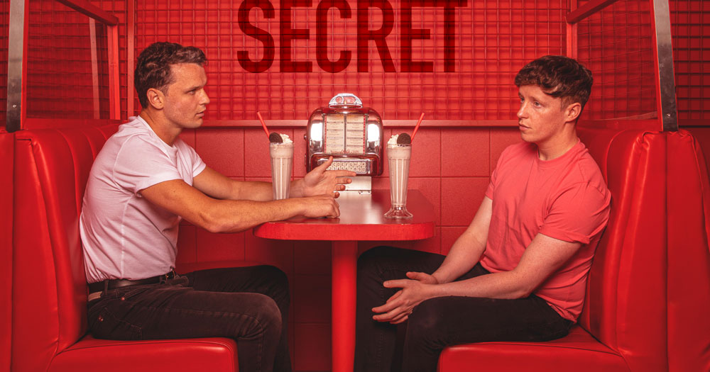 Poster of film How To Tell A Secret, releasing in Irish cinemas soon. Two men sitting at a diner with red walls and seats.