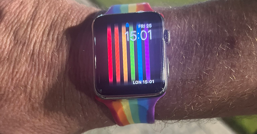 An Apple watch with a rainbow strap and rainbow background.