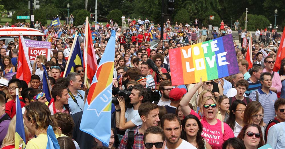 Crowd of people carrying LGBTQ+ Pride flags celebrate as US Senate passes same-sex marriage legislation.