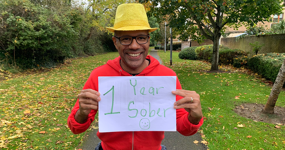 Marlon holds a sign saying '1 Year Sober'.