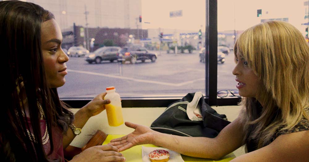Two women sit across from each other at a table in the movie, Tangerine, for this article that celebrates trans films.