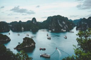 An areal photograph of Halong Bay in Vietnam. The bay is surrounded by high mountains and and there are a large number of boats sailing in the bay.
