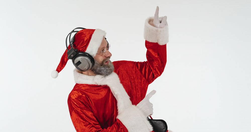 This article has a host of LGBTQ+ Christmas music to listen to. The photograph shows an elderly man in Santa costume, wearing headphones and dancing to music.