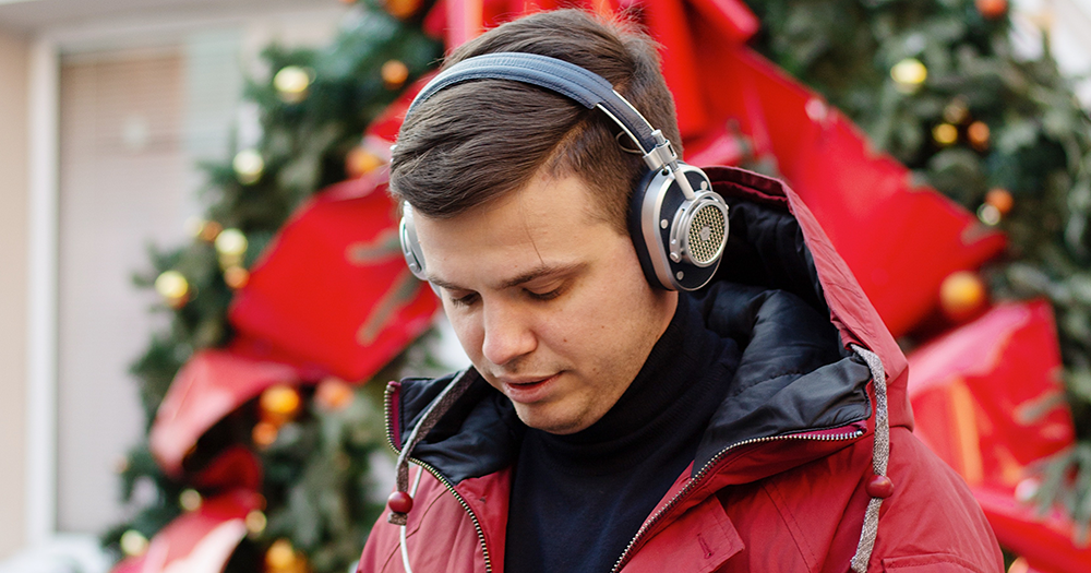 A person with headphones on in front of a Christmas wreath.