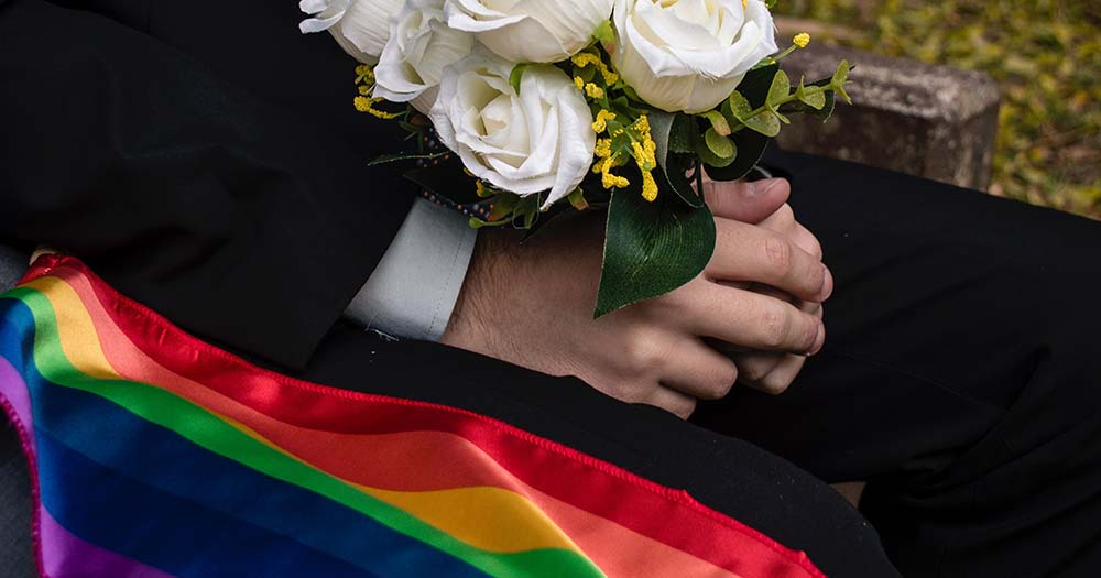 Pride flag sitting next to white hands holding white flowers because the DHS issued a domestic terrorism warning to LGBTQ+ people in wake of recent attacks.