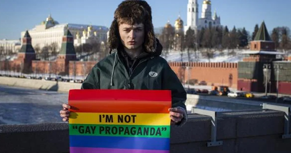 This article is about an anti-LGBTQ+ bill signed into Russian law. In the photo, a person standing and holding a sign that features the rainbow flag with the words “I’m not Gay Propoganda,” written on it.