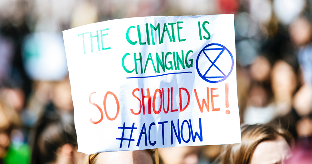 A protest sign reading "THE CLIMATE IS CHANGING SO SHOULD WE! #ACTNOW"
