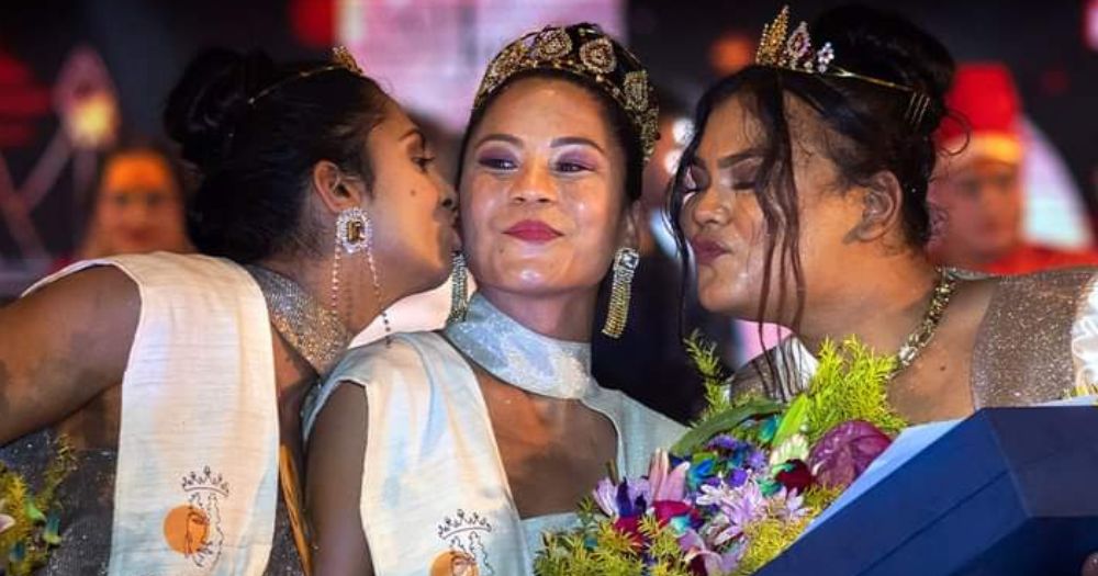 Northeastern India trans contestants Aria Deka, and Rishidhya Sangkarishan kiss the crowned victor Lucey Ham on stage as they hold flowers and wear crowns in traditional Indian garb.