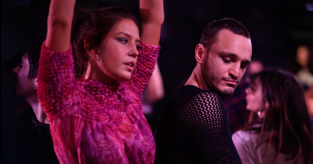Two characters from the queer film Passages, set to premiere at the 2023 Sundance Film Festival, dance close together in a nightclub with moody lighting.
