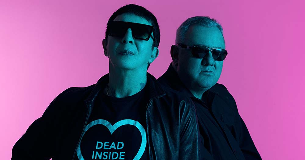 Members of the band Soft Cell pose in blue lighting with a pink background announcing that they will be performing in St Anne's Park on June 3!