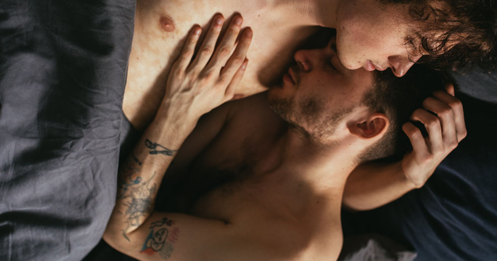 The image shows two men embraced in a bed. They are both topless with a bed sheet wrapped around their waists. The image is to promote the Squirt.org Christmas giveaway.