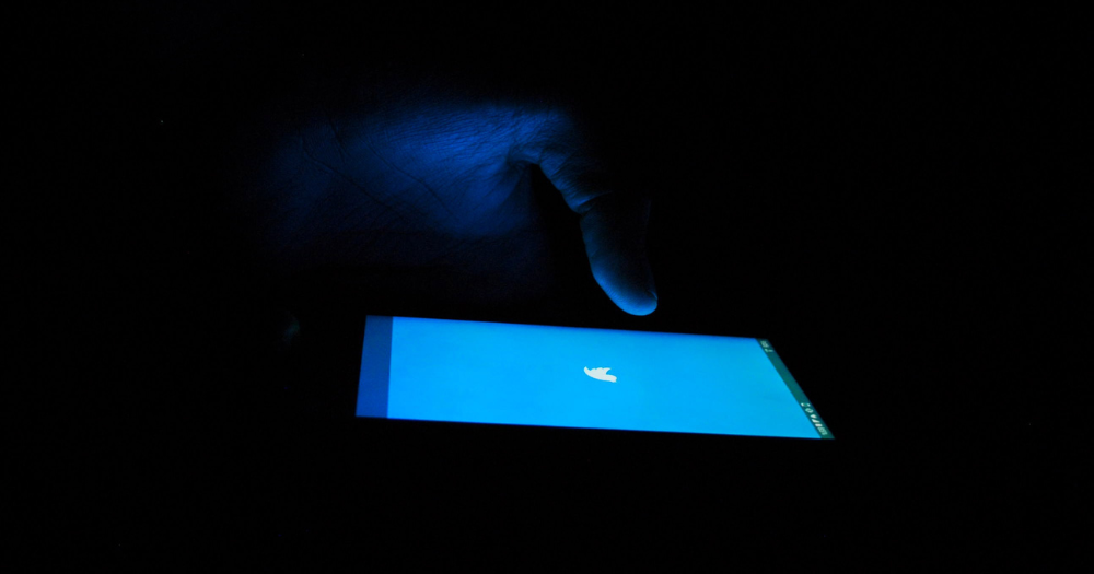 A person in a dark room opens Twitter on their device.