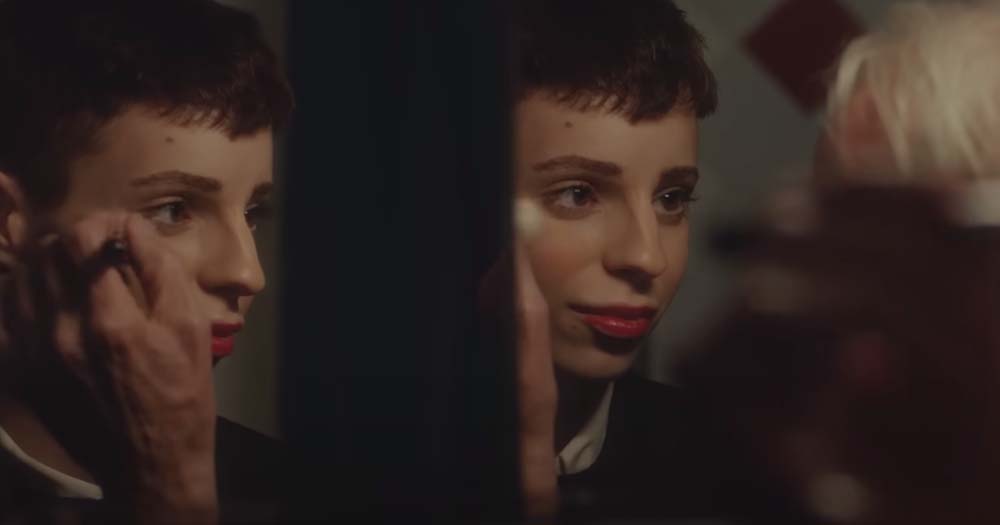 Reflection of trans granddaughter applying make-up in moving whiskey advertisement.