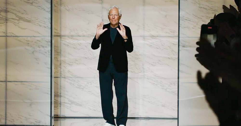 Giorgio Armani wearing black suit walks runway at fashion show before facing criticism for his comments surrounding non-heterosexual couples.