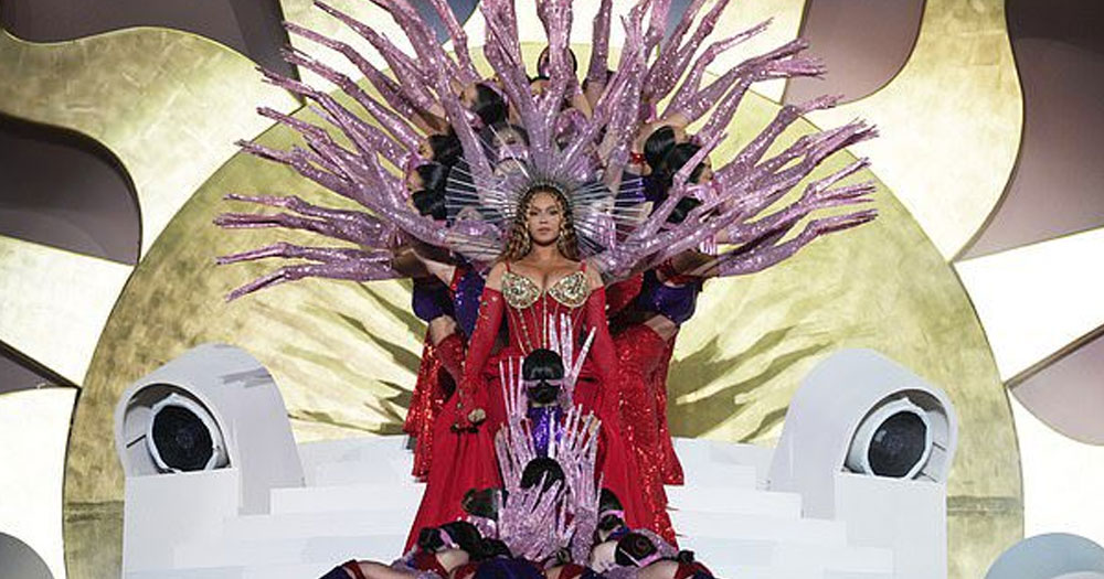 Still from the concert Beyoncé performed in Dubai. She is dressed in a red dress with pink decorations and dancers around her.