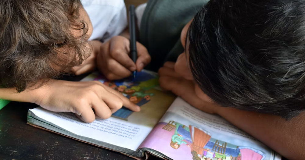 This article is about LGBTQ+ books for children. In the photo, two kids reading and scribbling on a book.
