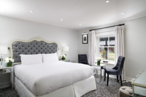 An image of a bedroom at the Lodge at Ashford Castle. The room and bedspread are white with a grey headboard.