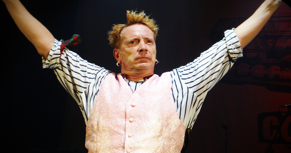 John Lydon with his arms raised on stage.