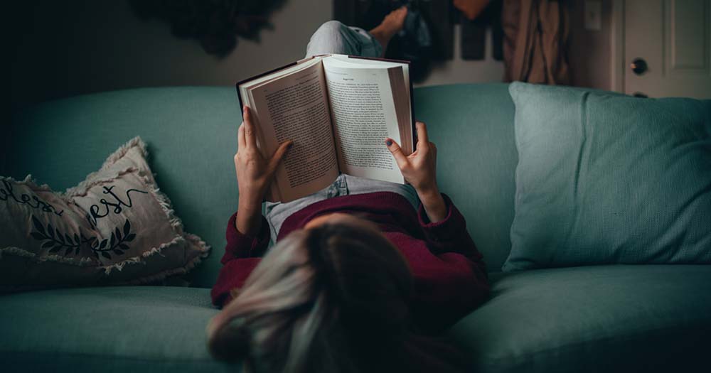 Woman with dark hair reads book on a couch previewing some LGBTQ+ books to read in 2023.