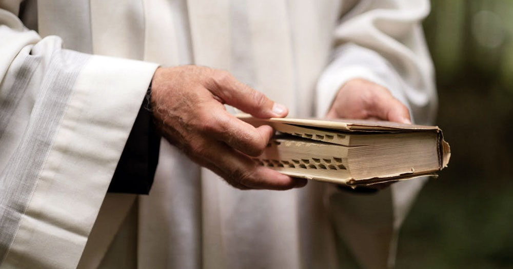 This article is about the Church of England voting to offer blessings for same-sex unions. In the photo, the bands of a priest holding a bible.