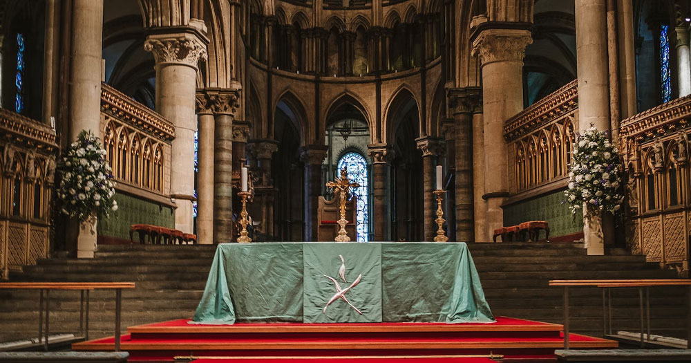 This article is about a debate in the Church of England over the use of gender-neutral language in reference to God. In the photo, an altar with a golden cross on top, inside of a church.