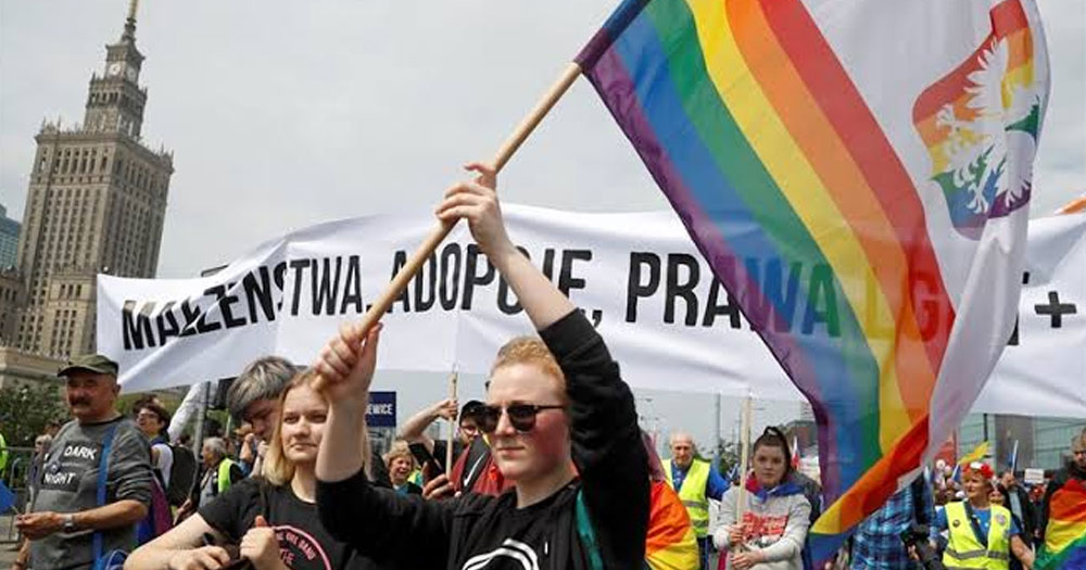 This article si about the EU closing a legal case against Poland. In the photo, LGBTQ+ activists marching in Warsaw, flying Pride flags and carrying banners.