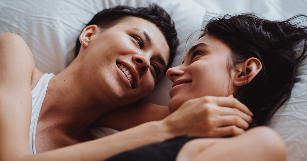 An LGBTQ+ couple smiling in bed.