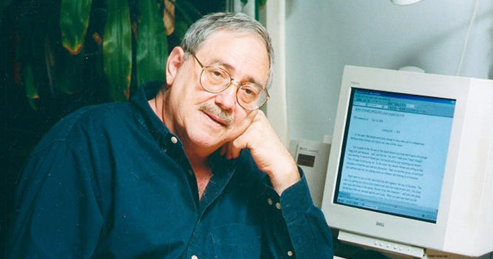 Dr. Charles Silverstein wearing a green shirt and glasses next to a computer.