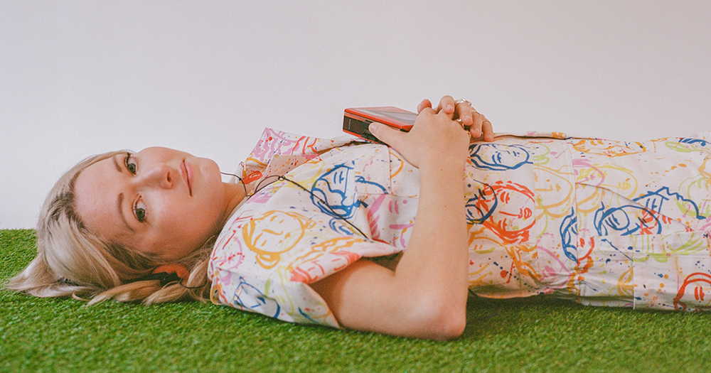 Ailbhe Reddy wearing a colourful dress and laying on a green rug, she is performing in Whelan's on May 5th and 6th, and GCN has a signed album and a pair of tickets to give away to a lucky reader!