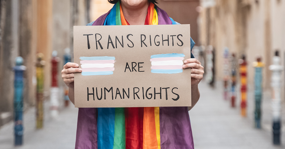 Person wearing rainbow flag across shoulders and carrying a trans rights are humans rights sign after Kentucky passed worst anti-trans bill in U.S.