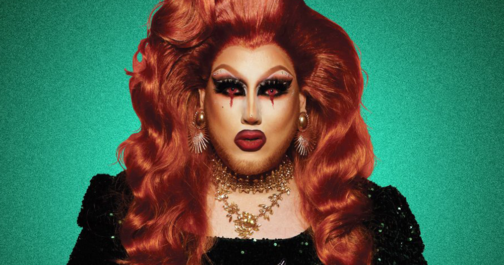 Irish Drag Queen Lavender with red hair and bold make up stands in front of a green background