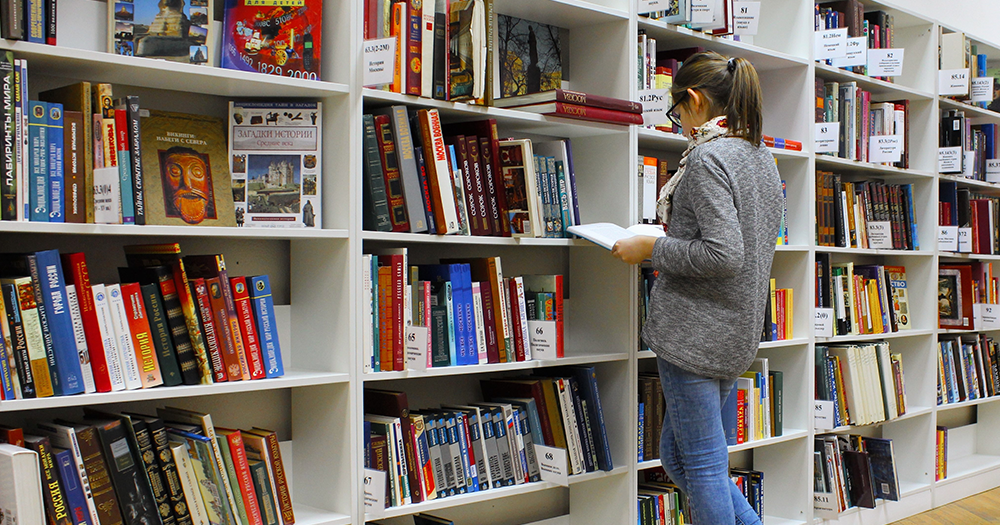 A woman facing a bookshelf representing US book ban attempts across US public schools and libraries.