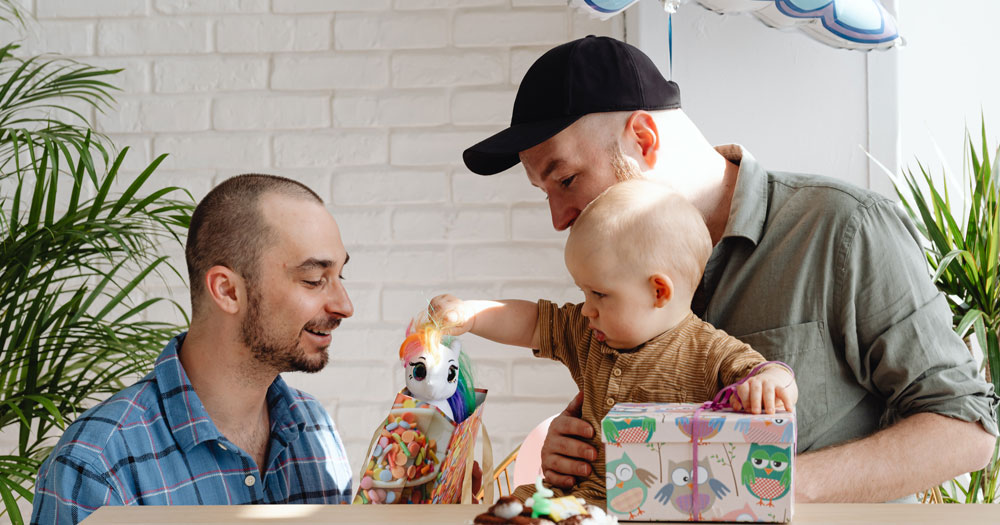 This article is about same-sex parents in Milan. In the photo, two men holding a baby during a birthday party.