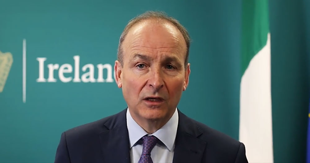 Tánaiste Micheál Martin, who recently address the US crackdown on LGBTQ+ rights, speaking to the public while standing in front of a green background with the word Ireland.